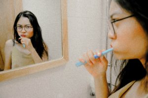 Woman looking in mirror brushing teeth after visiting dentist near Love Field.
