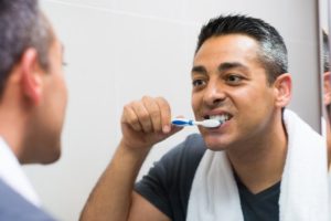 Man looking in the mirror and brushing his teeth with a towel behind his neck