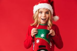 A little girl in a Santa hat holding a Christmas stocking and smiling