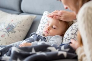 Mother resting her hand on her sick daughter’s forehead while she sleeps