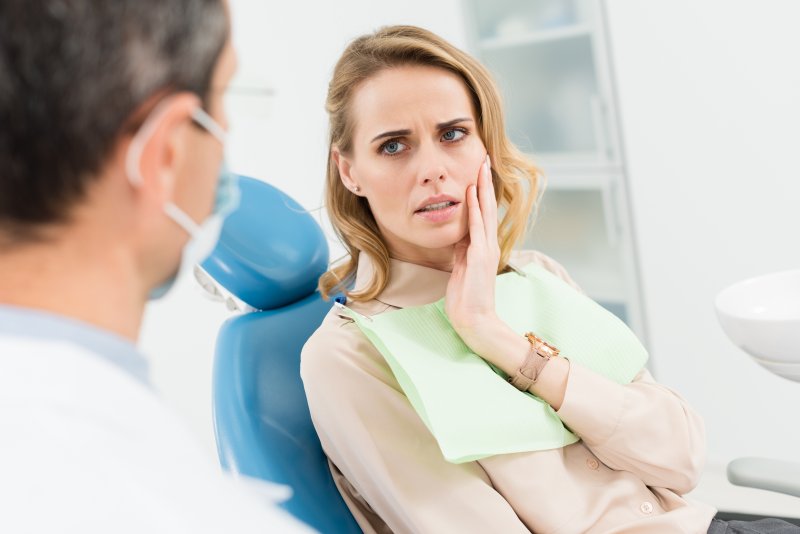woman with toothache in Love Field holding cheek at dentist 