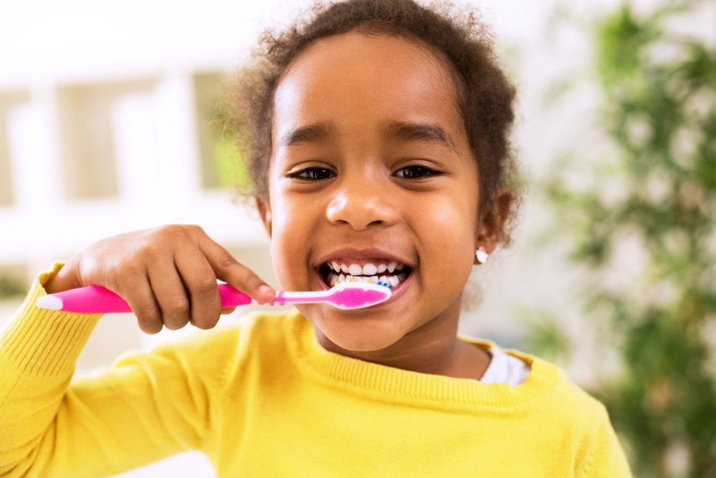 Closeup of girl in yellow shirt brushing her teeth