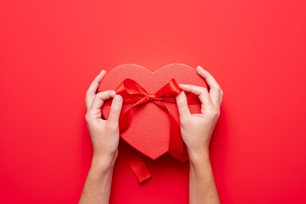 Person wrapping red bow on heart box