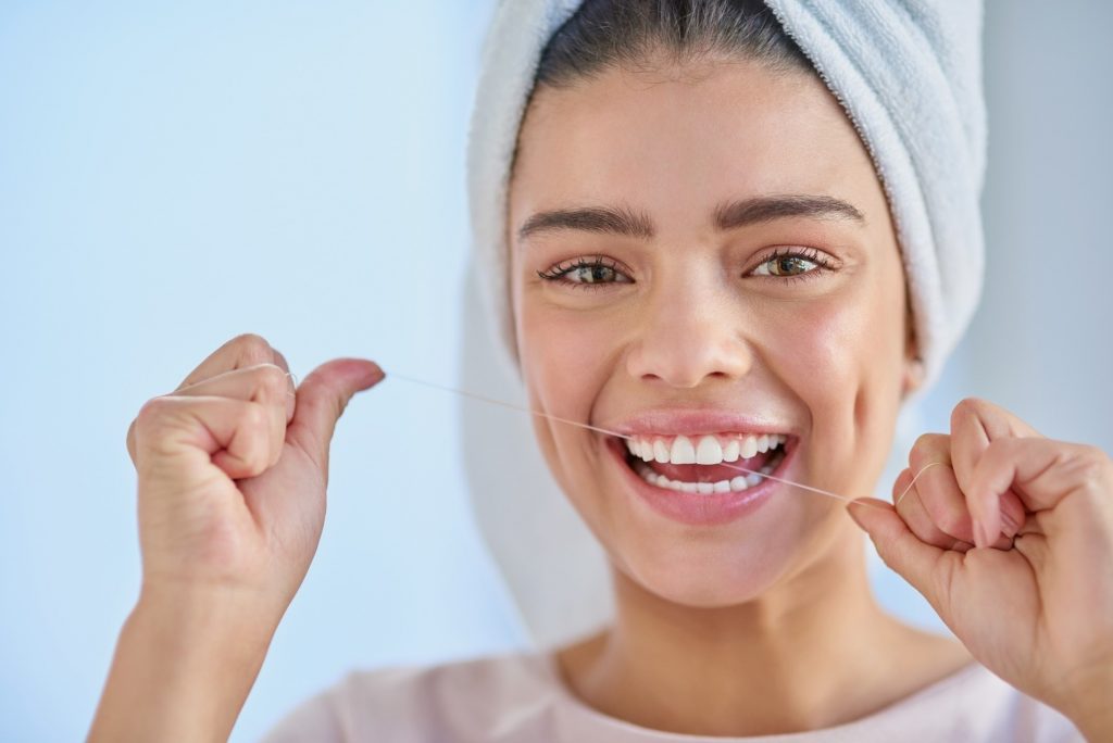Smiling woman with white teeth flossing in bathroom