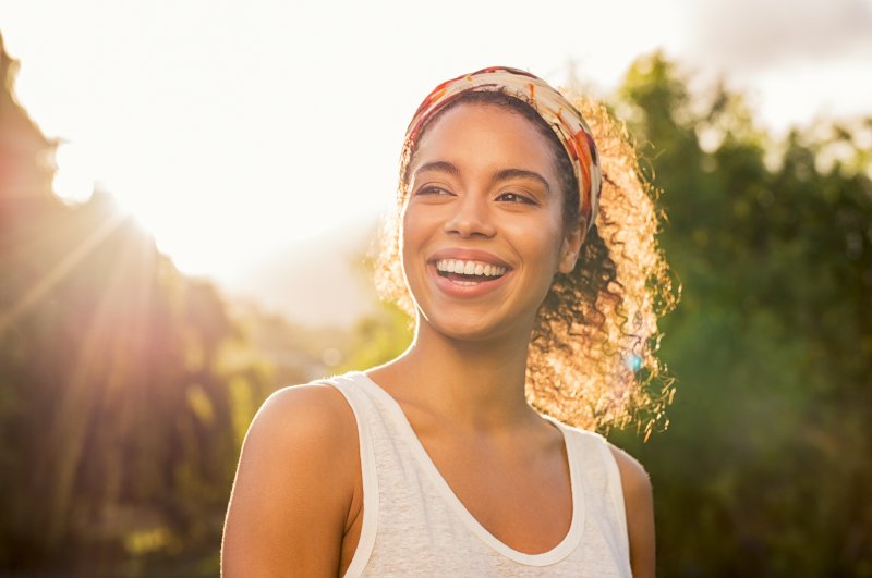 Woman wearing headband smiles with teeth outside in the summer sun