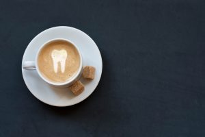 Birds eye view of a white cup of coffee on a white saucer with 2 cubes of brown sugar with a tooth design in the coffee foam