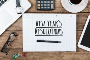 Lined paper with New Year's Resolutions on a wooden surface with other office items