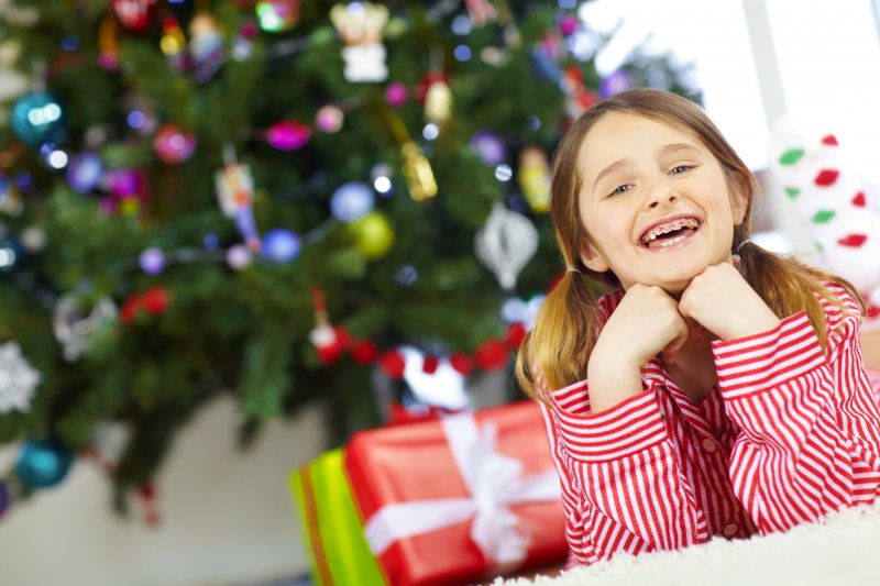 A small girl with braces smiling under a holiday tree