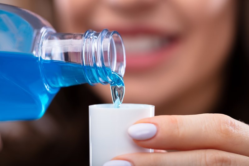 A blurred woman pouring mouthwash into a cup