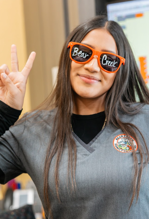 Dental technician giving peace sign and smiling while wearing sunglasses with "Bear Creek" written on them