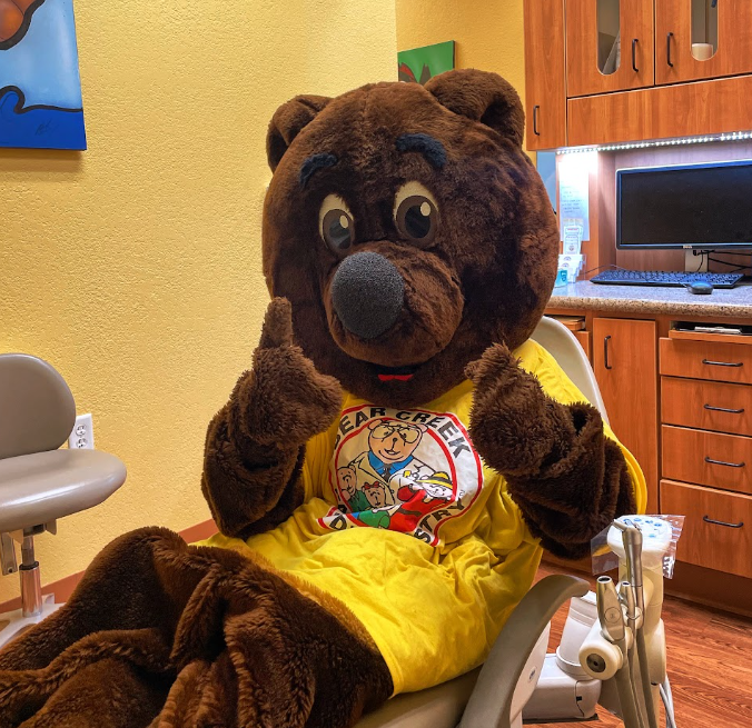 Bear mascot in dental chair doing finger guns